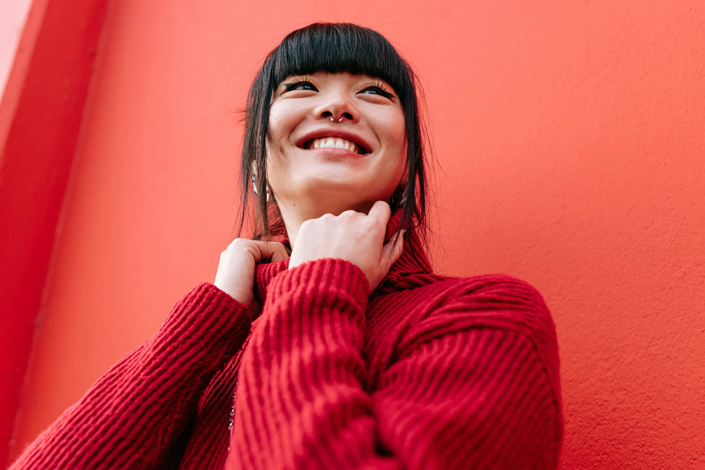 Woman with a nose ring smiling against a bright red wall