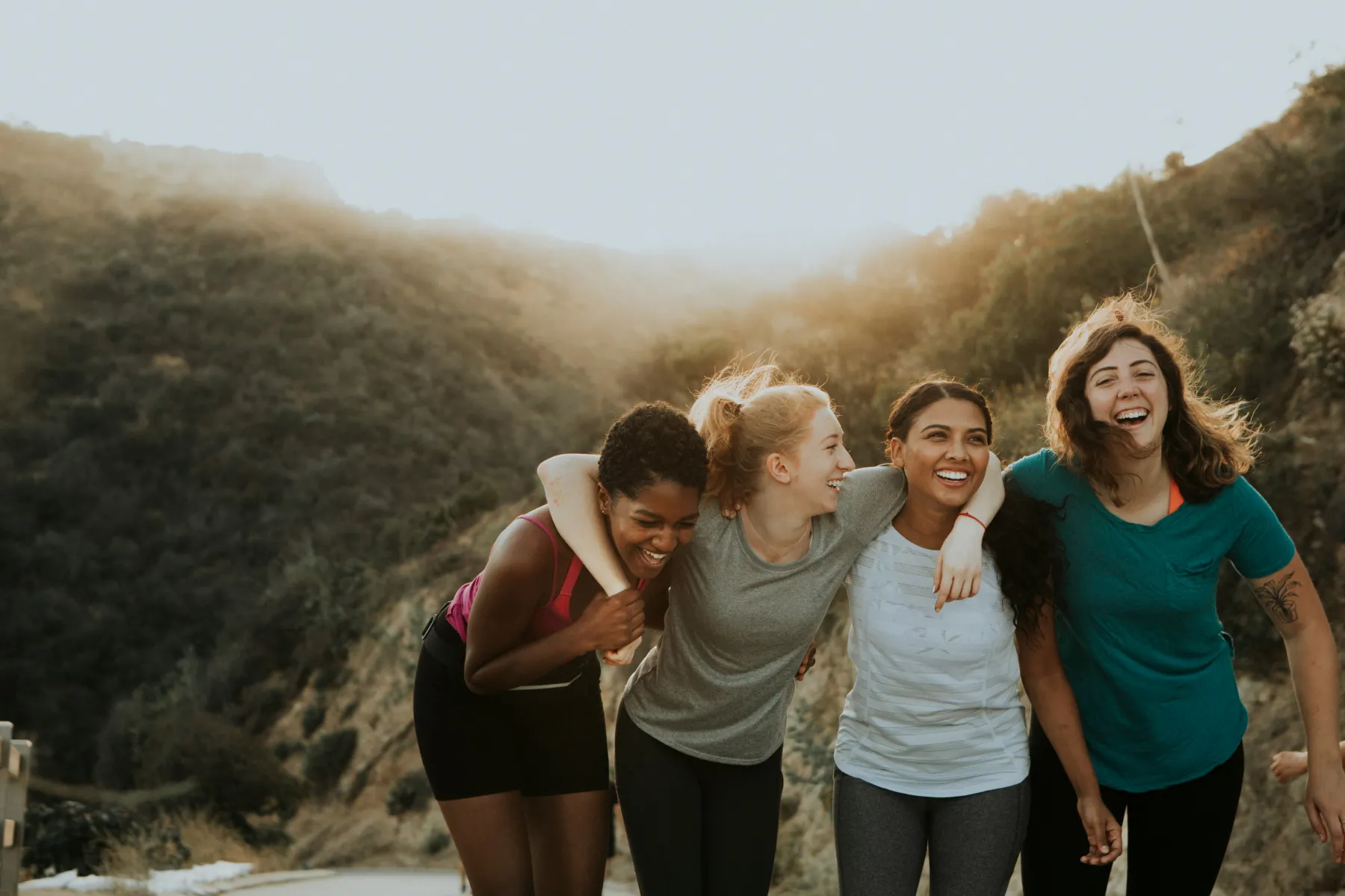 Four women arm in arm laughing on a sunny hillside