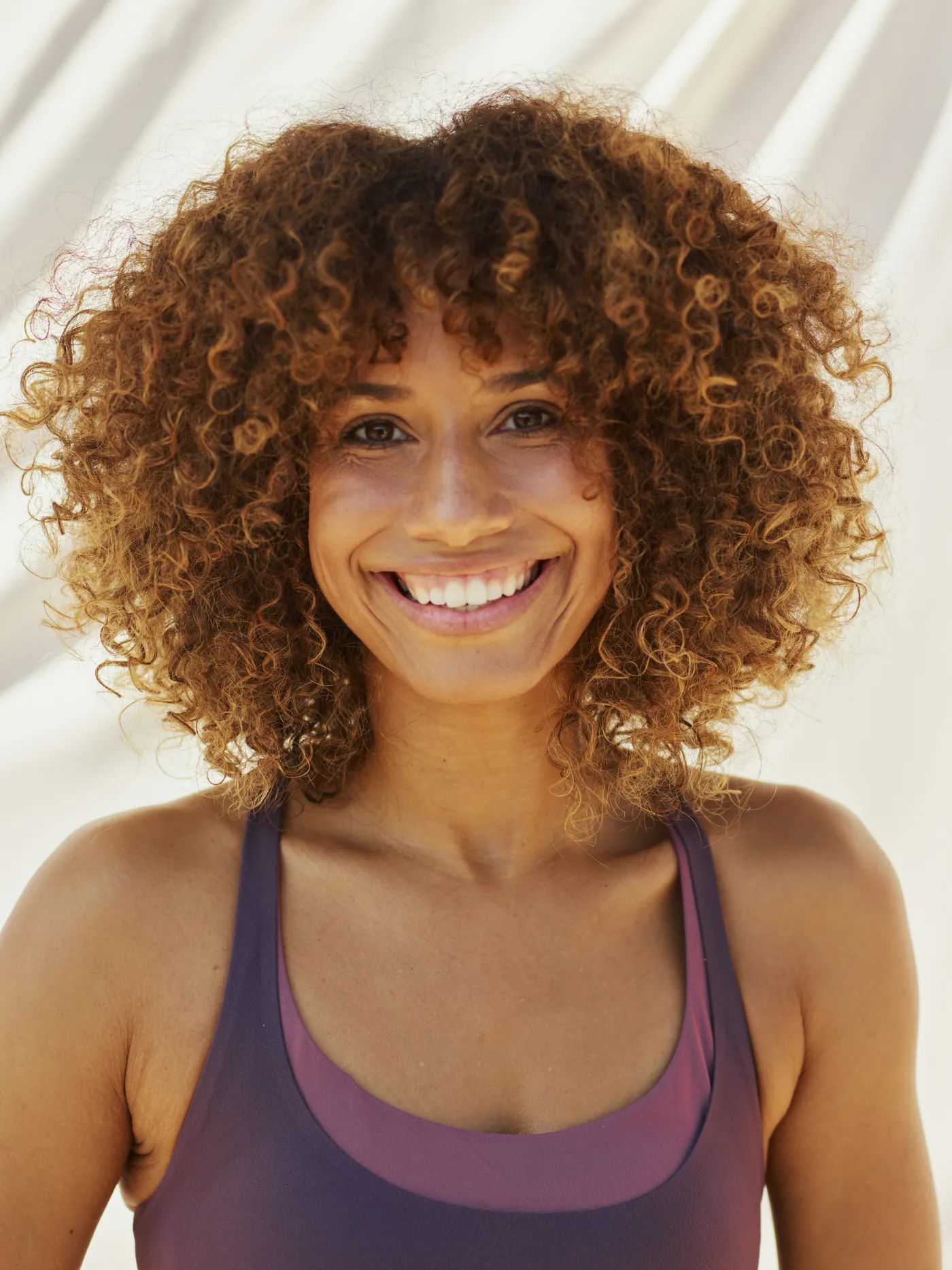 A smiling woman with curly hair in a purple sports top