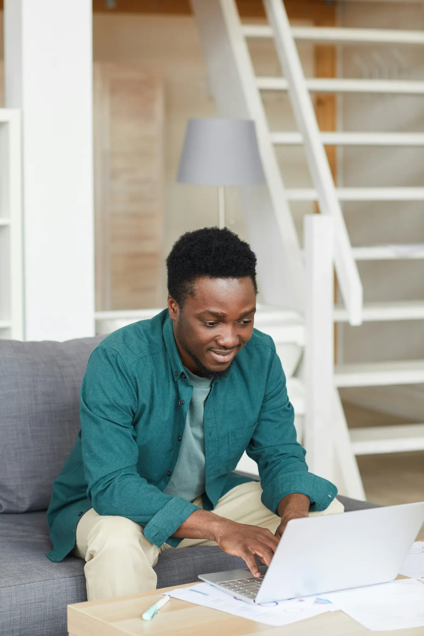 A man in a teal shirt smiling at his laptop during a video session at home